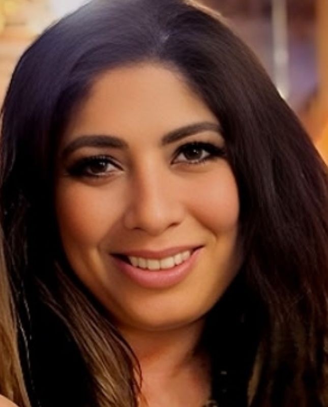 Smiling person with long dark hair in a warmly lit environment.